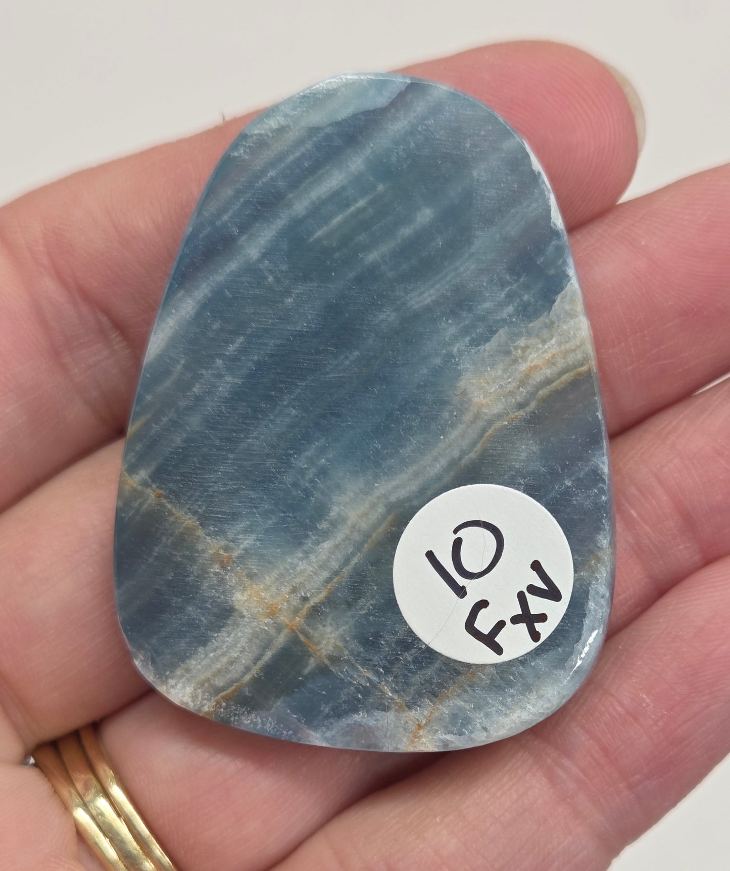 Blue Onyx cabochon with yellow veins held in a hand against a white background