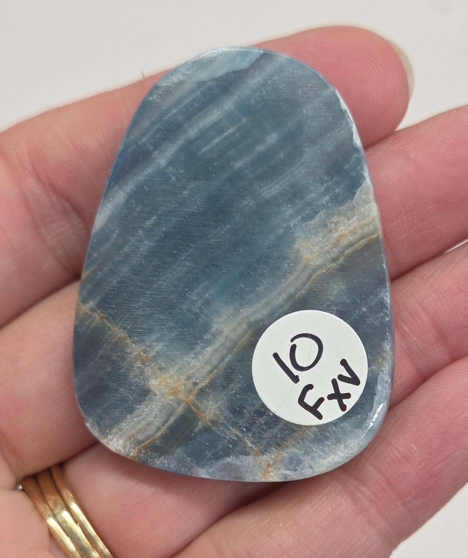Blue Onyx cabochon with yellow veins held in a hand against a white background