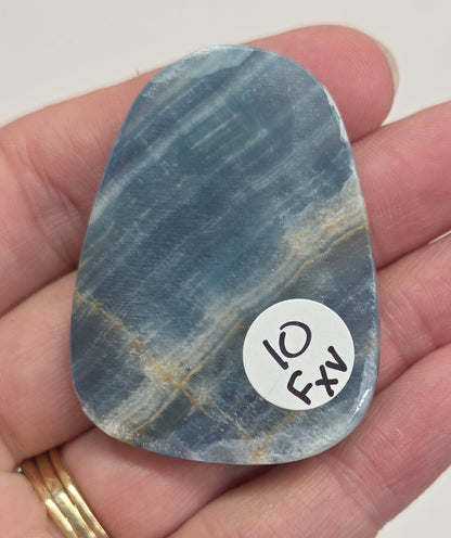 Blue Onyx cabochon with yellow veins held in a hand against a white background