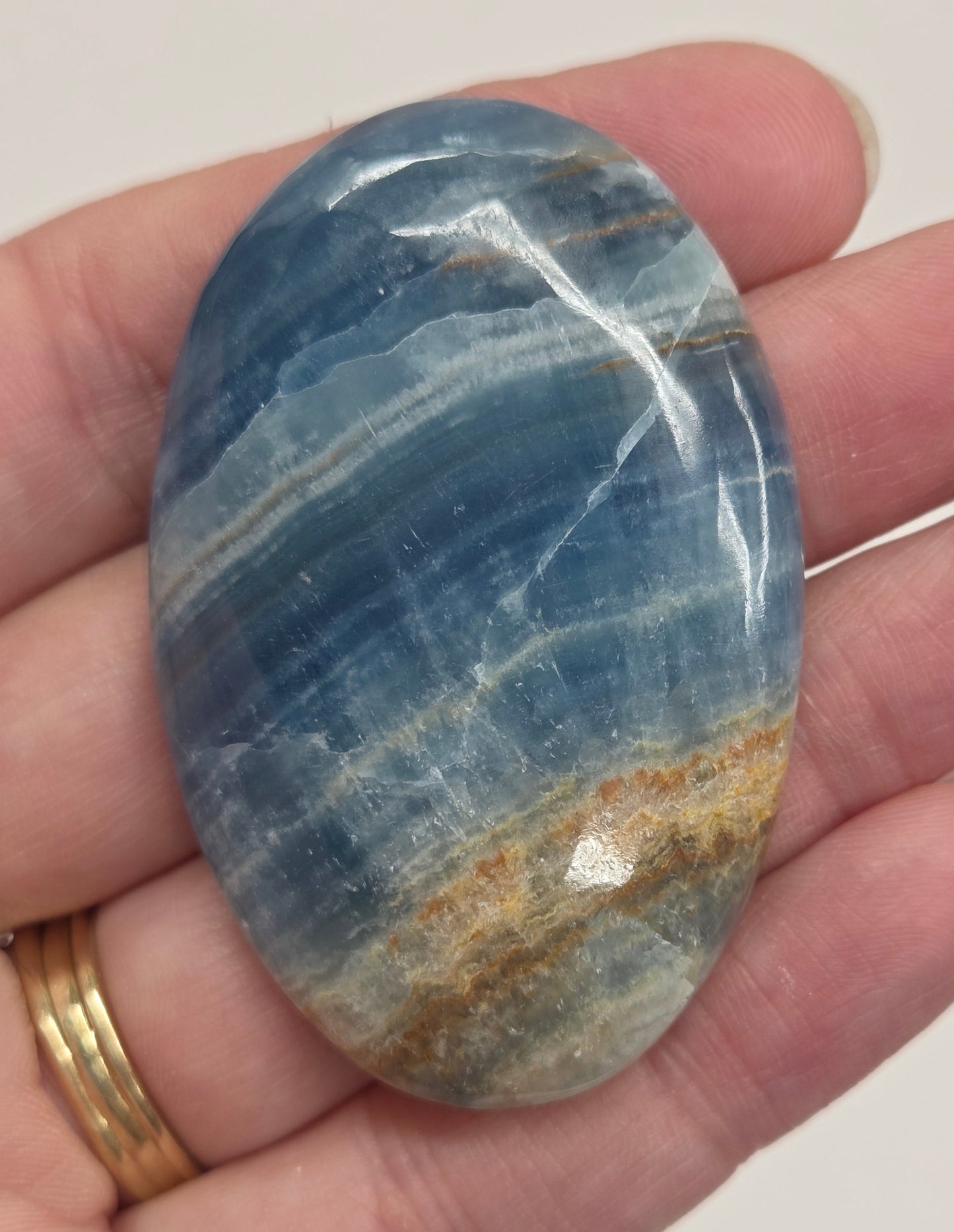 Blue Onyx cabochon with yellow veins held in a hand against a white background