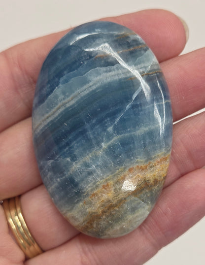 Blue Onyx cabochon with yellow veins held in a hand against a white background