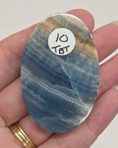 Blue Onyx cabochon with yellow veins held in a hand against a white background