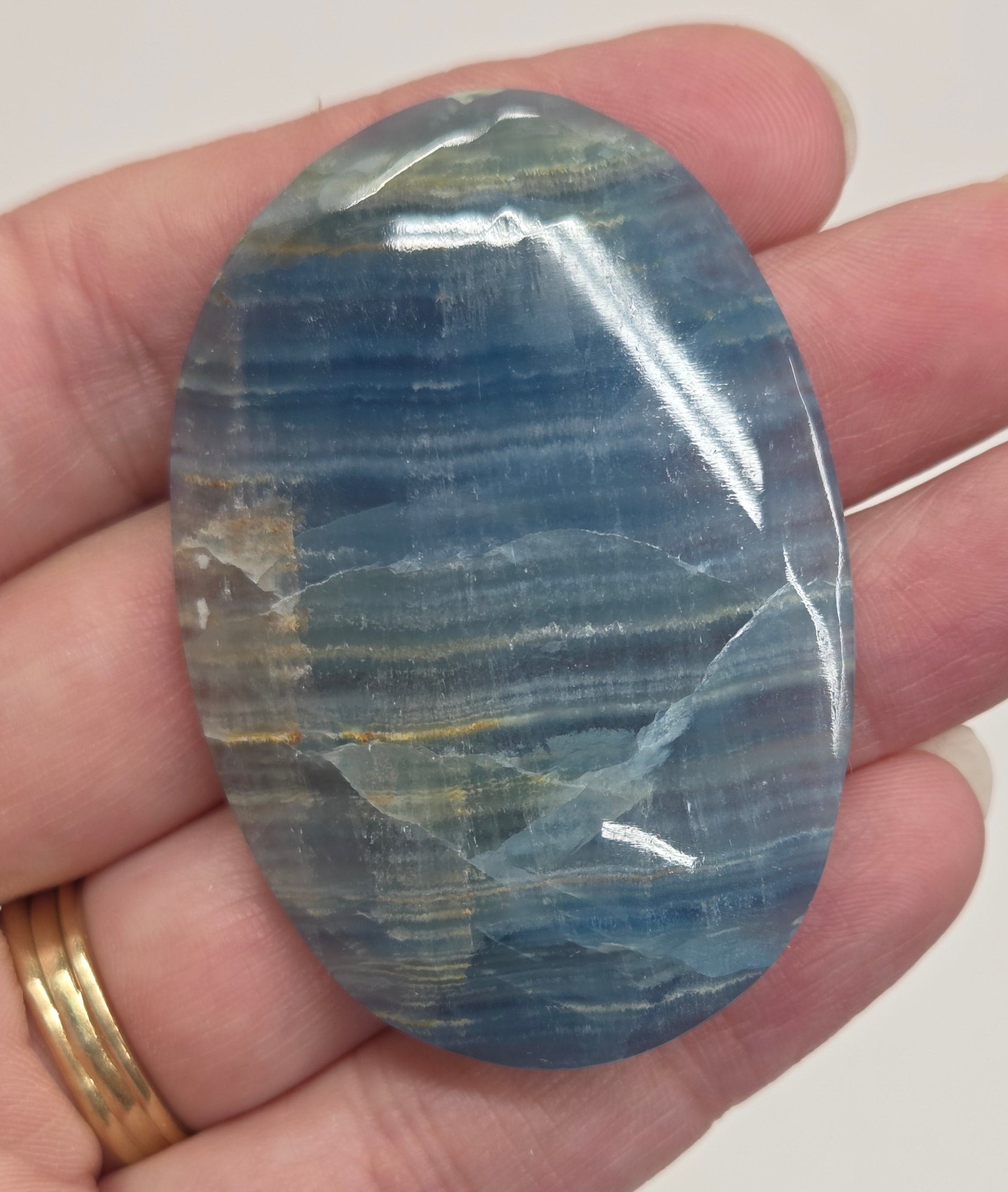 Blue Onyx cabochon with yellow veins held in a hand against a white background