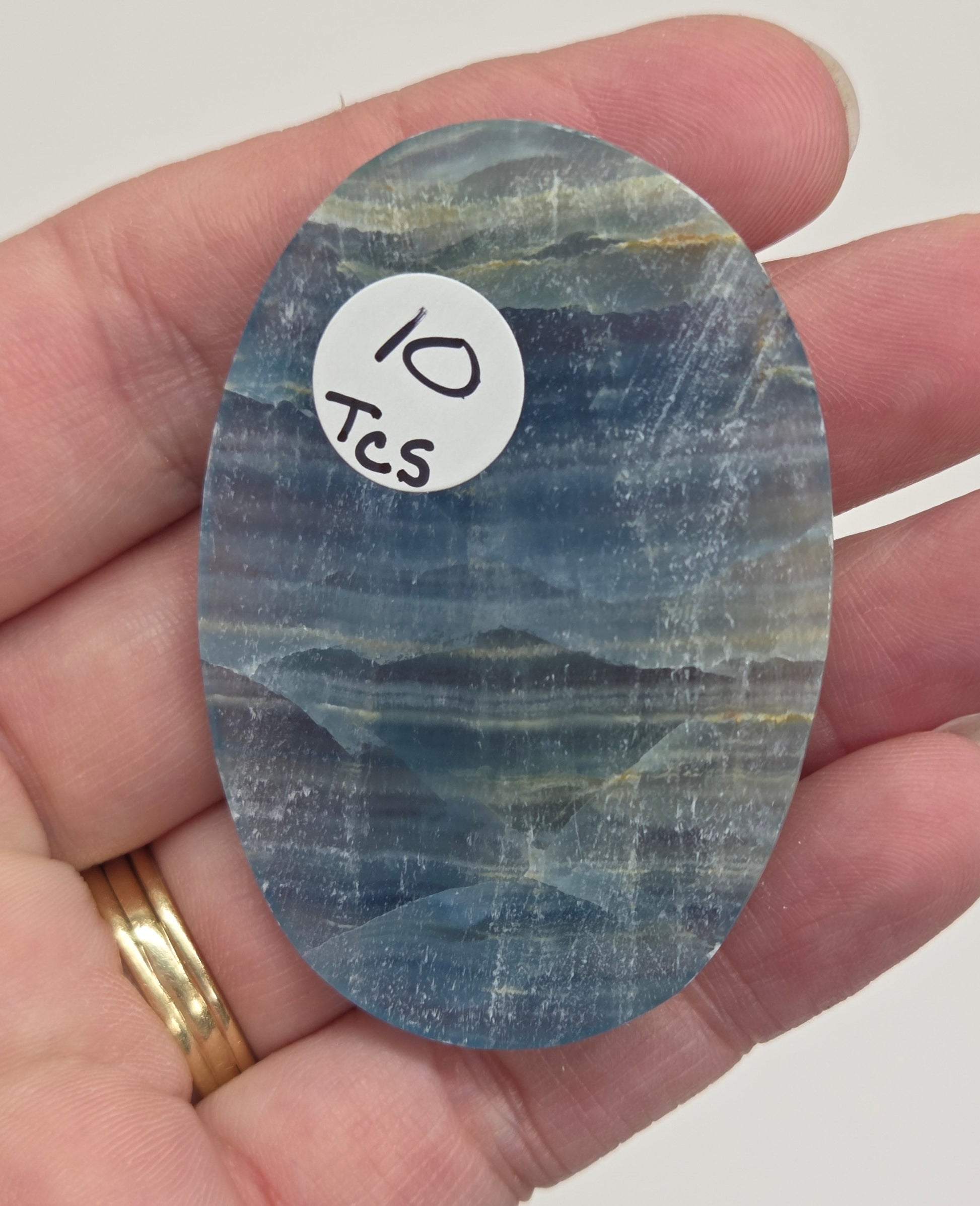 Blue Onyx cabochon with yellow veins held in a hand against a white background