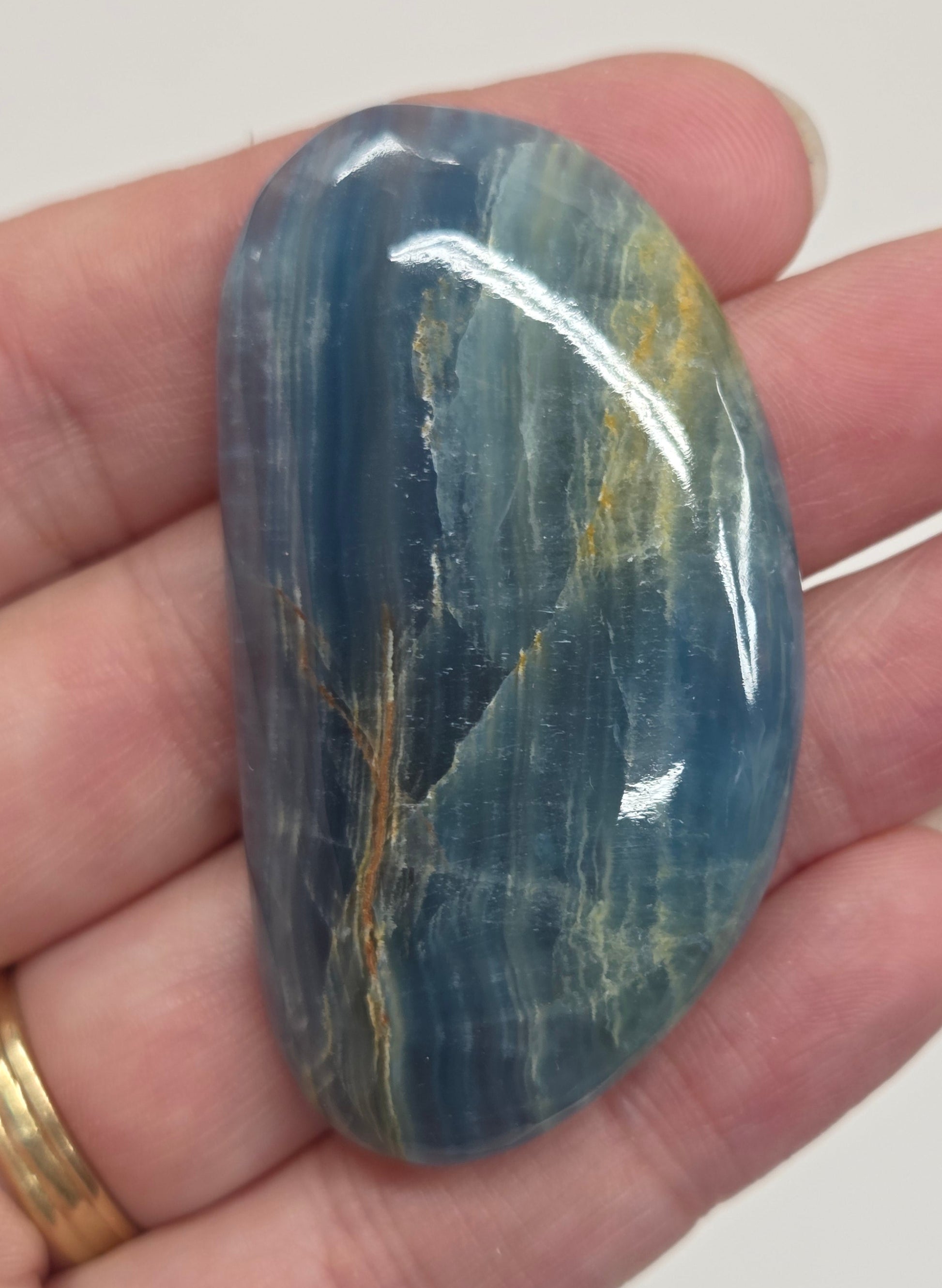 Blue Onyx cabochon with yellow veins held in a hand against a white background