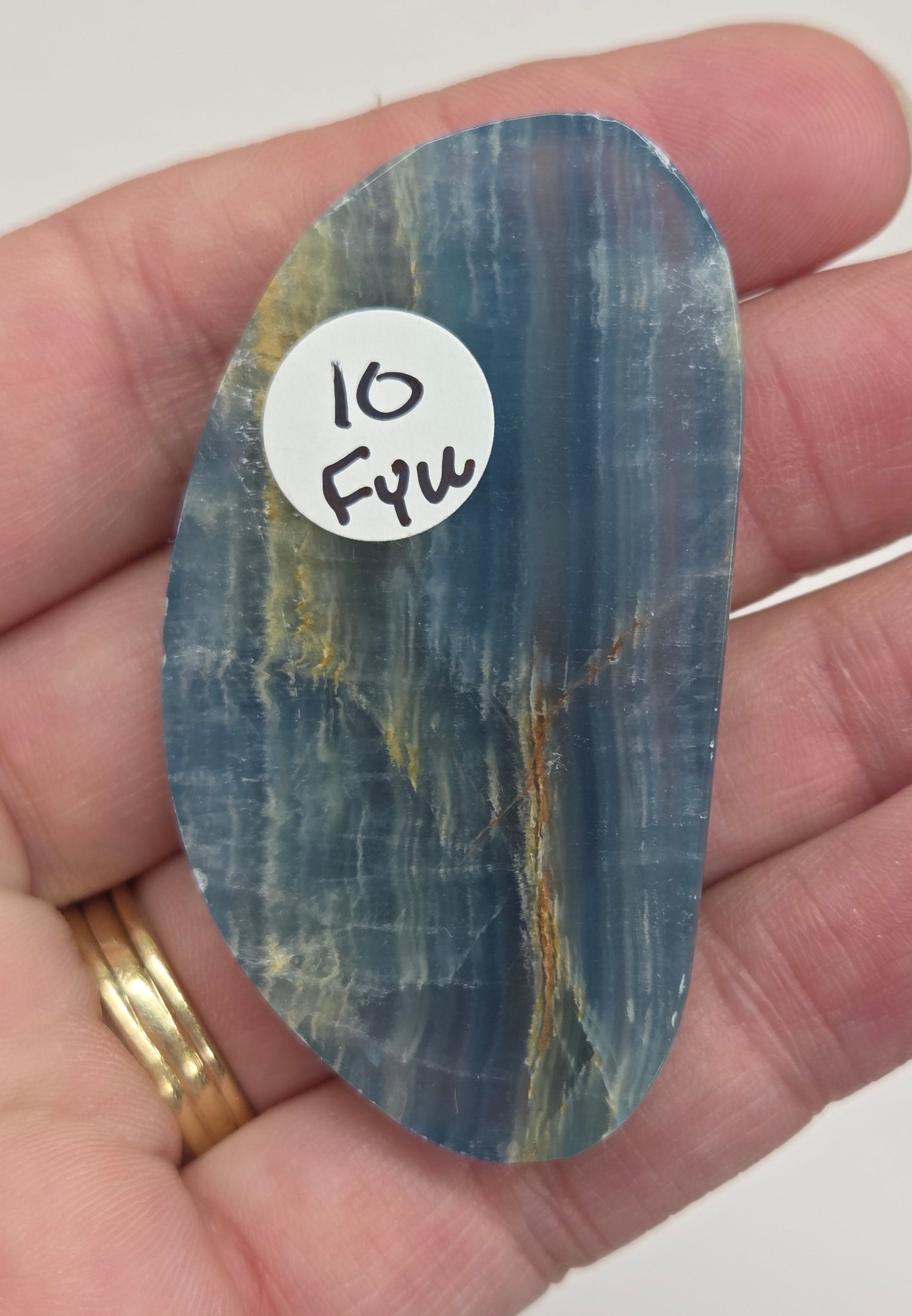 Blue Onyx cabochon with yellow veins held in a hand against a white background