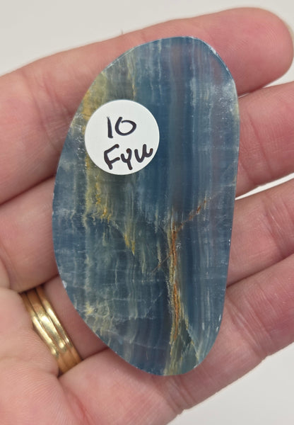 Blue Onyx cabochon with yellow veins held in a hand against a white background