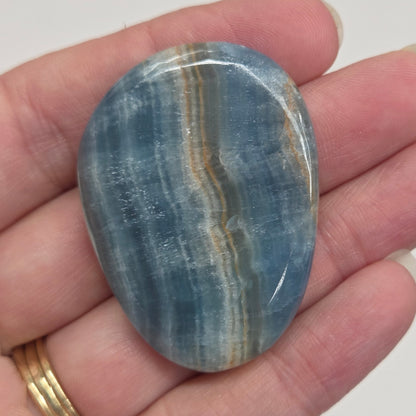 Blue Onyx cabochon with yellow veins held in a hand against a white background