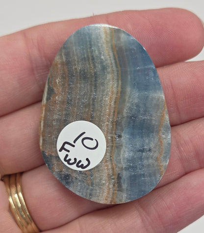 Blue Onyx cabochon with yellow veins held in a hand against a white background