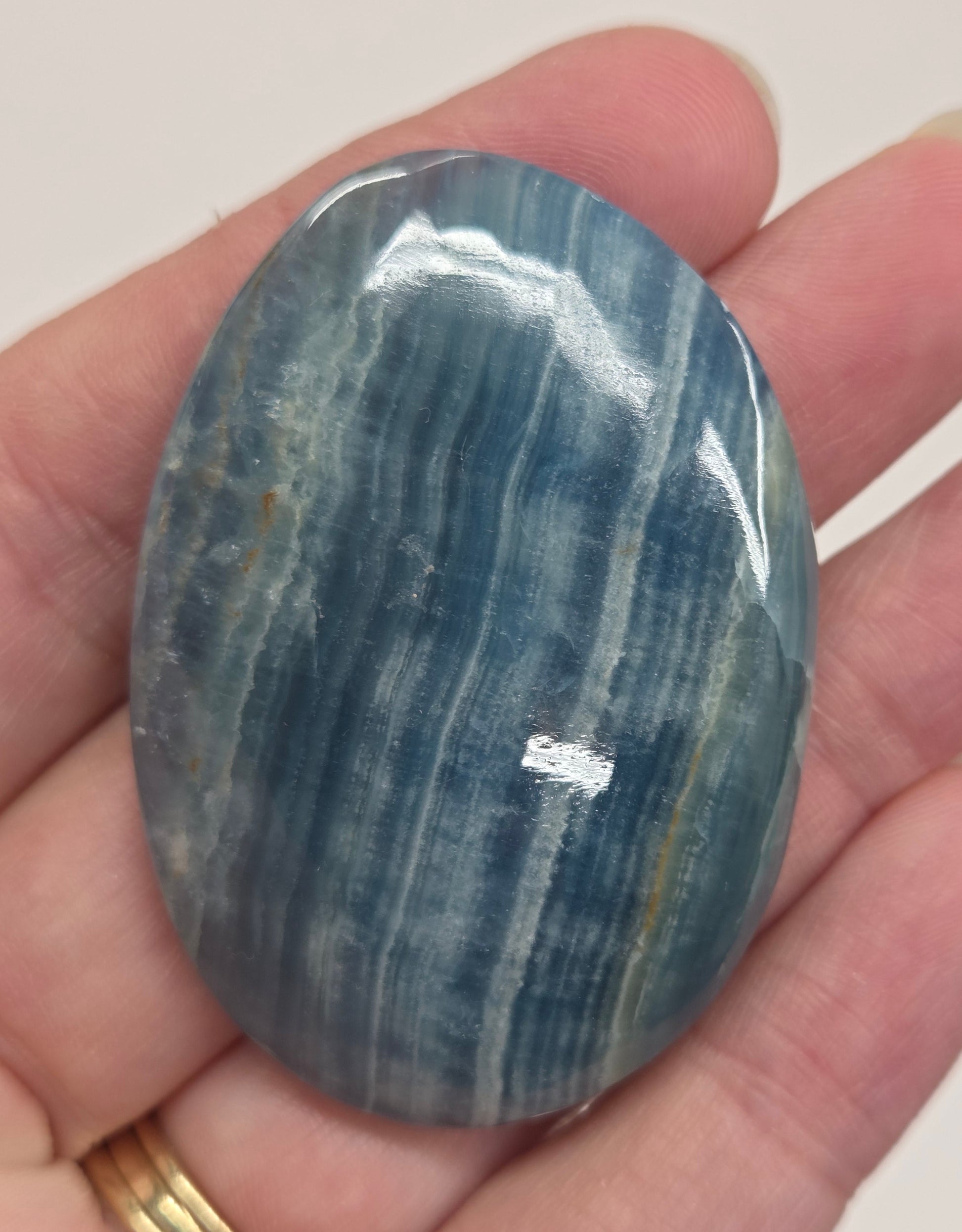 Blue Onyx cabochon with yellow veins held in a hand against a white background