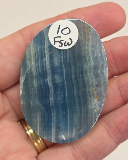 Blue Onyx cabochon with yellow veins held in a hand against a white background