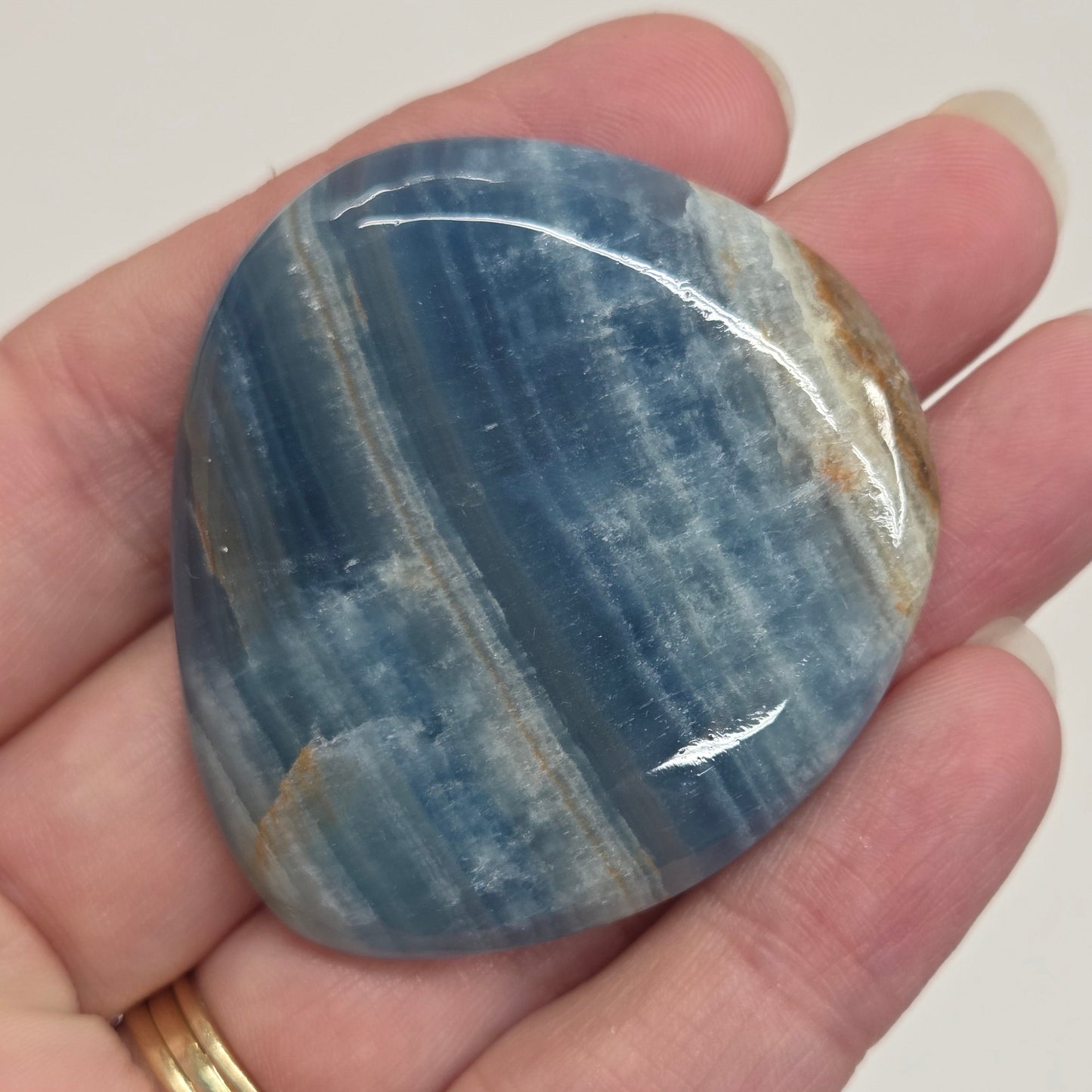 Blue Onyx cabochon with yellow veins held in a hand against a white background