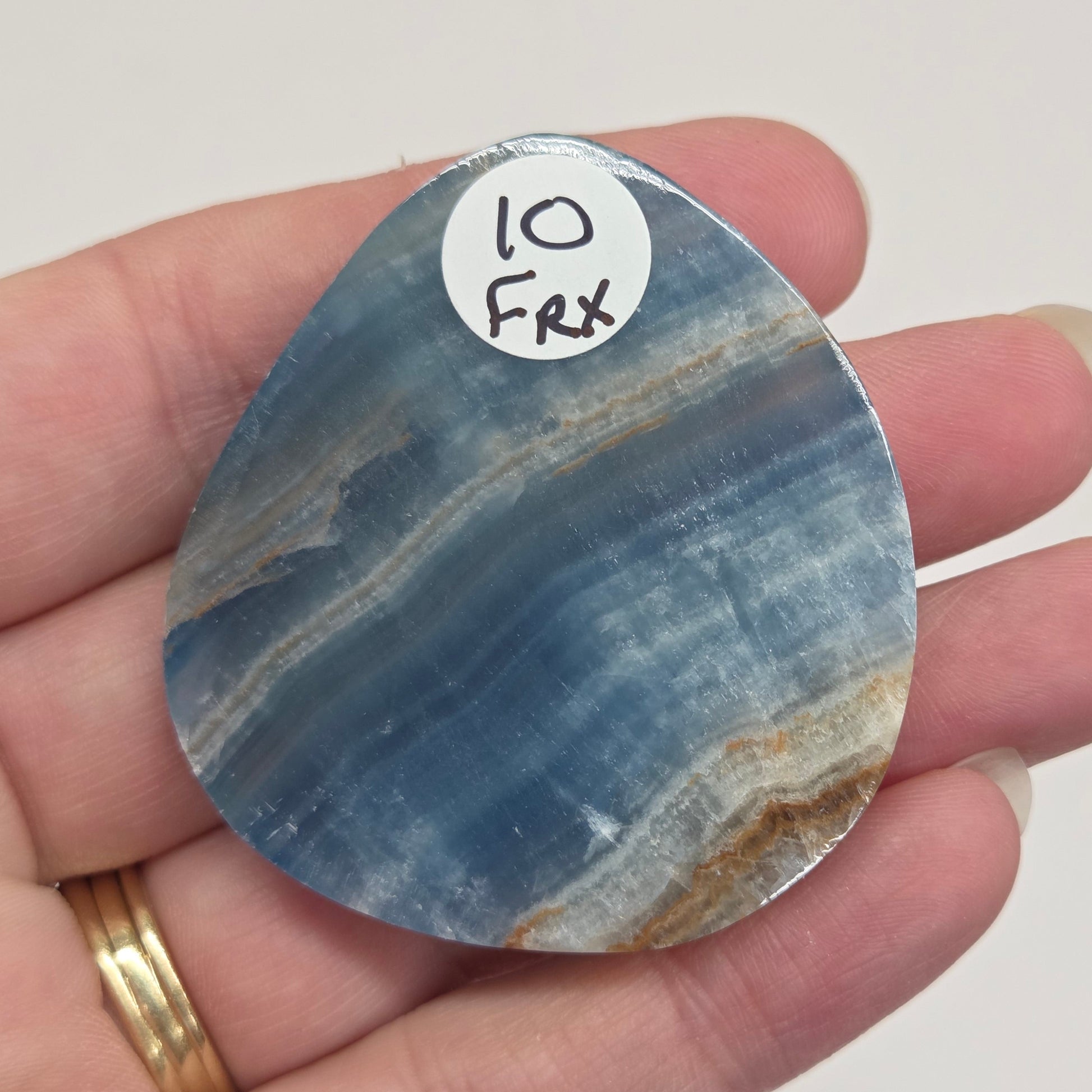 Blue Onyx cabochon with yellow veins held in a hand against a white background
