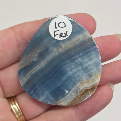 Blue Onyx cabochon with yellow veins held in a hand against a white background