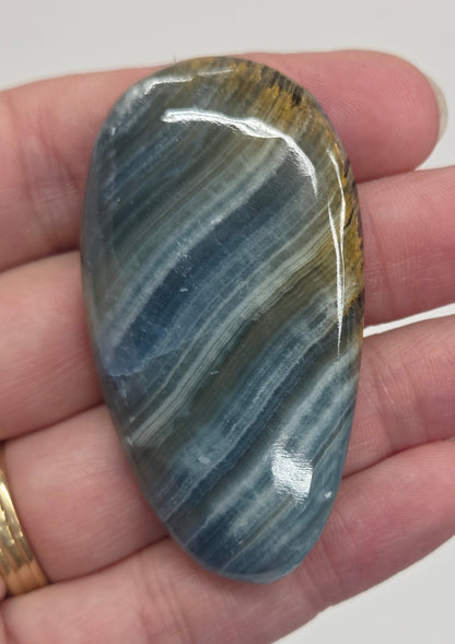 Blue Onyx cabochon with yellow veins held in a hand against a white background