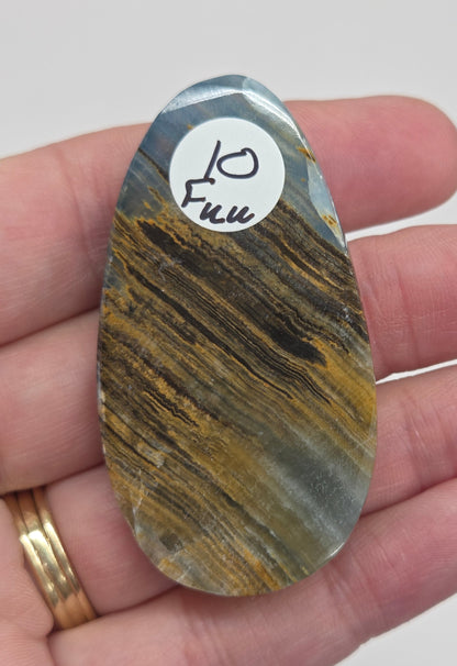 Blue Onyx cabochon with yellow veins held in a hand against a white background
