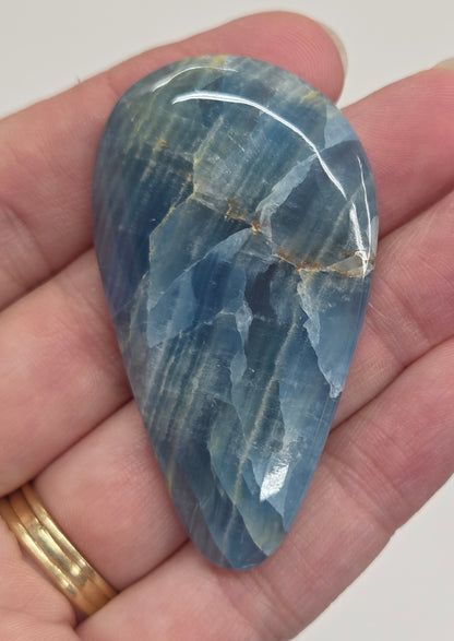 Blue Onyx cabochon with yellow veins held in a hand against a white background