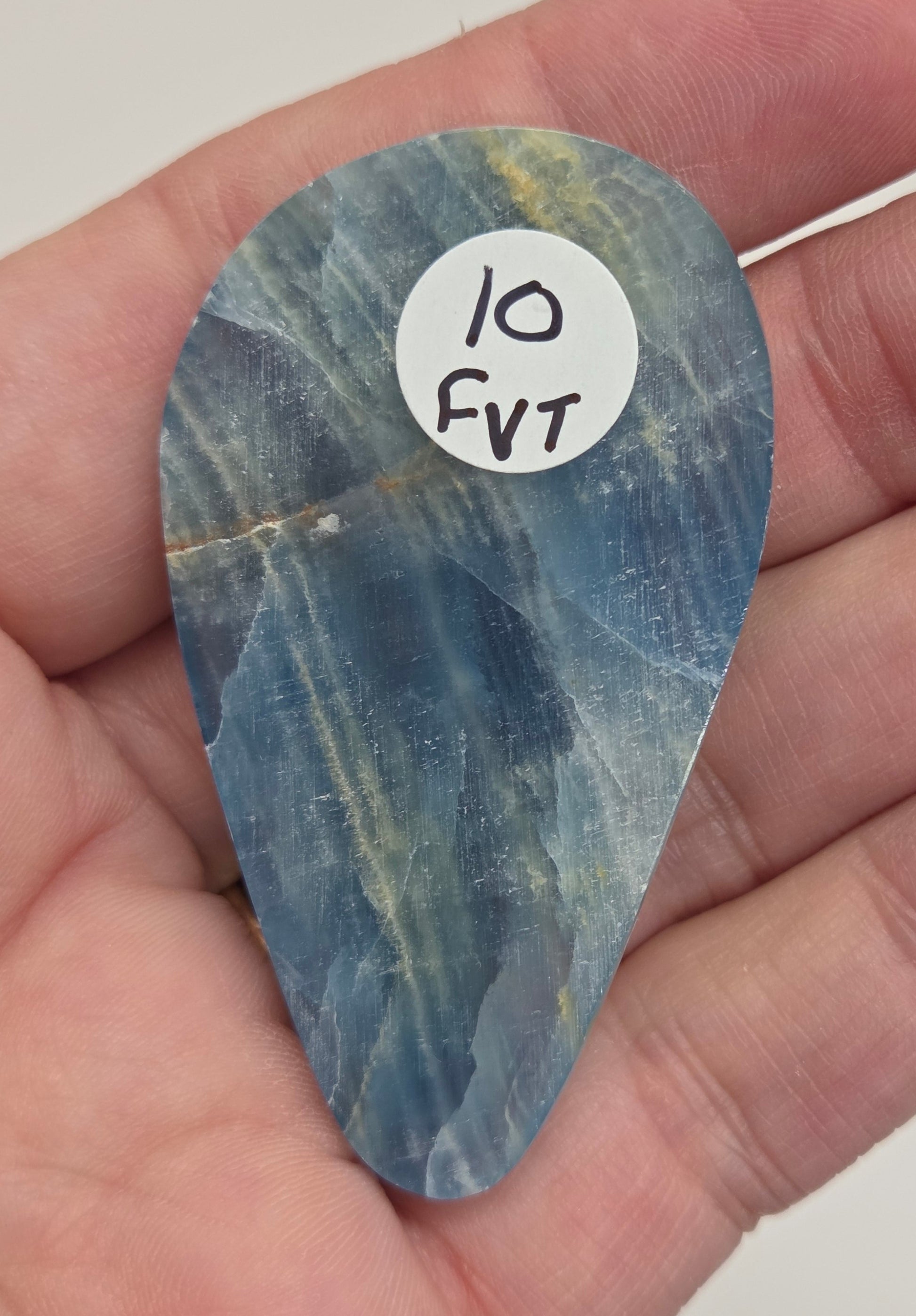 Blue Onyx cabochon with yellow veins held in a hand against a white background