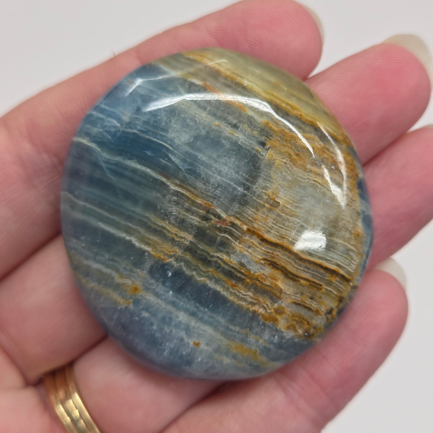 Blue Onyx cabochon with yellow veins held in a hand against a white background