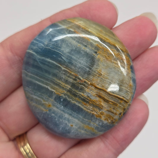 Blue Onyx cabochon with yellow veins held in a hand against a white background
