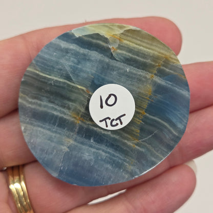 Blue Onyx cabochon with yellow veins held in a hand against a white background