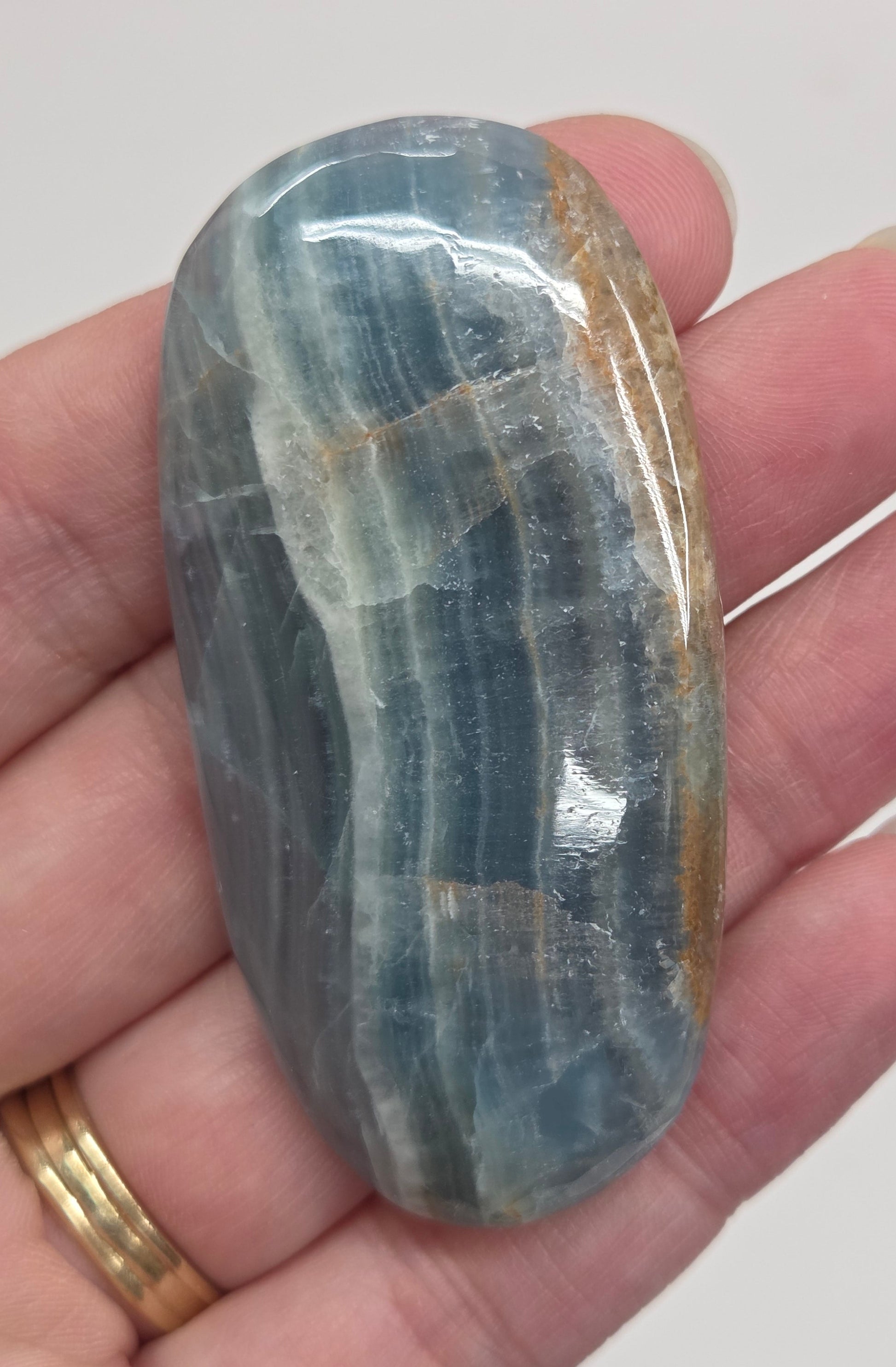 Blue Onyx cabochon with yellow veins held in a hand against a white background