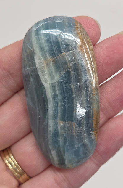 Blue Onyx cabochon with yellow veins held in a hand against a white background