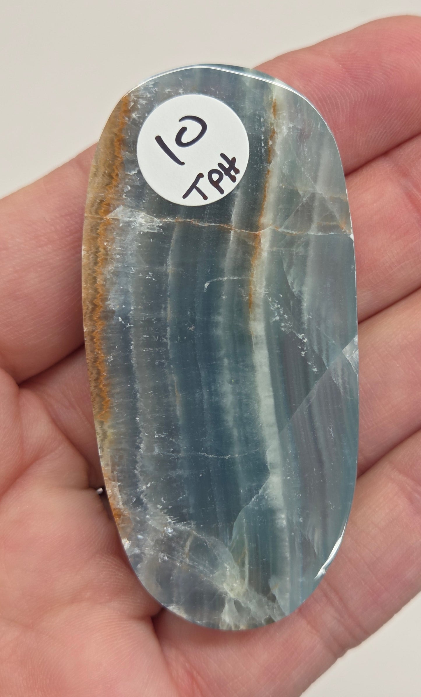 Blue Onyx cabochon with yellow veins held in a hand against a white background