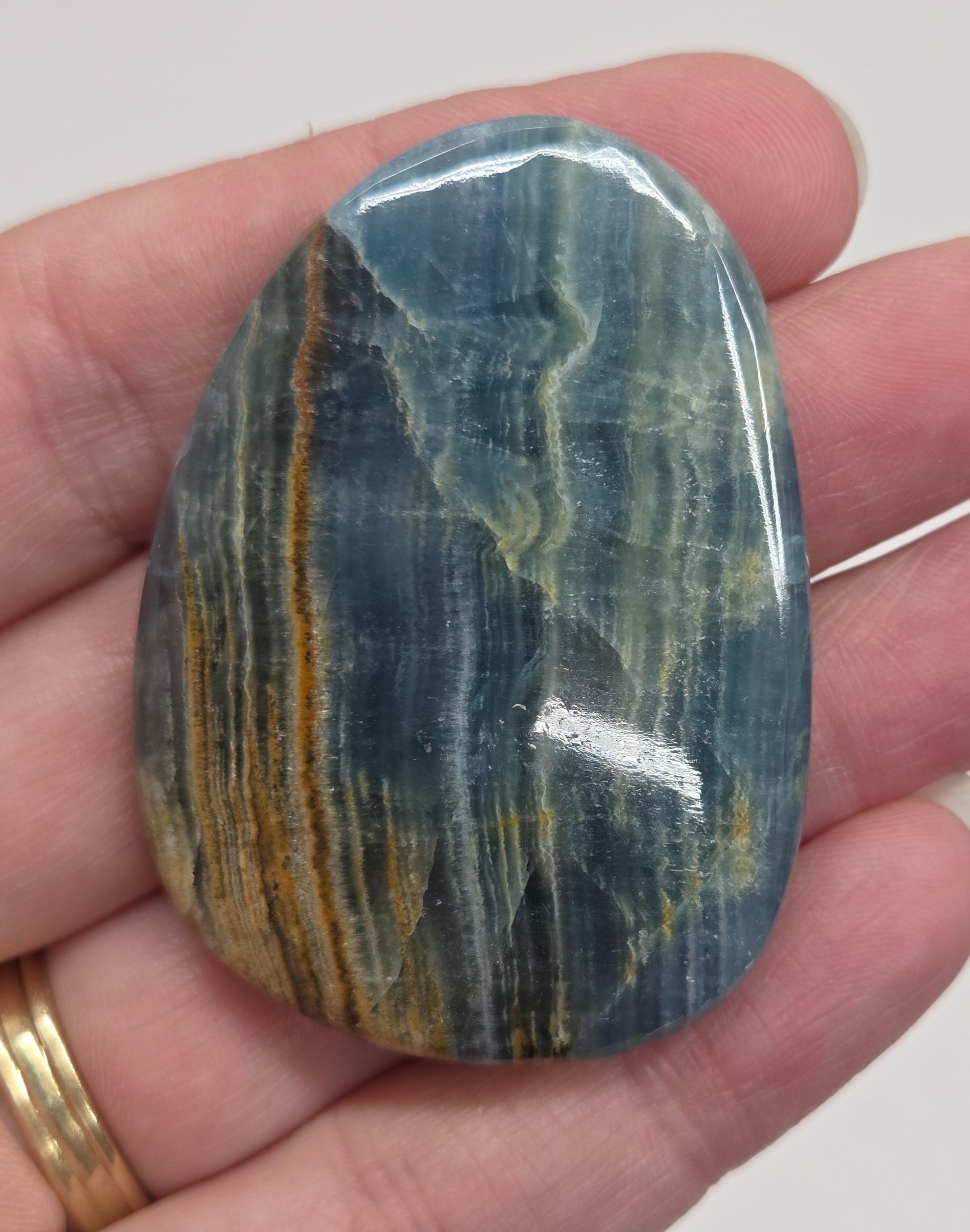 Blue Onyx cabochon with yellow veins held in a hand against a white background