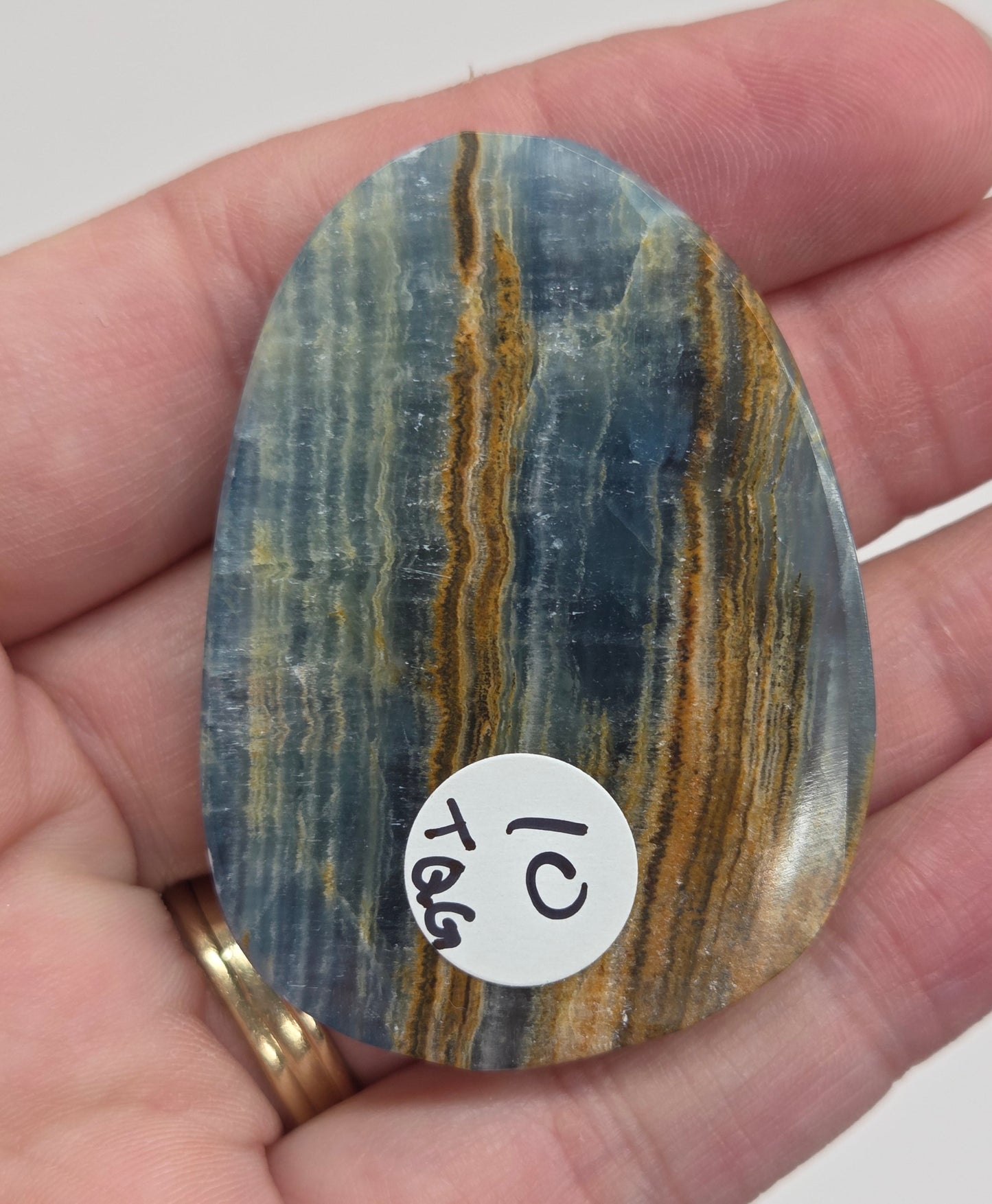 Blue Onyx cabochon with yellow veins held in a hand against a white background