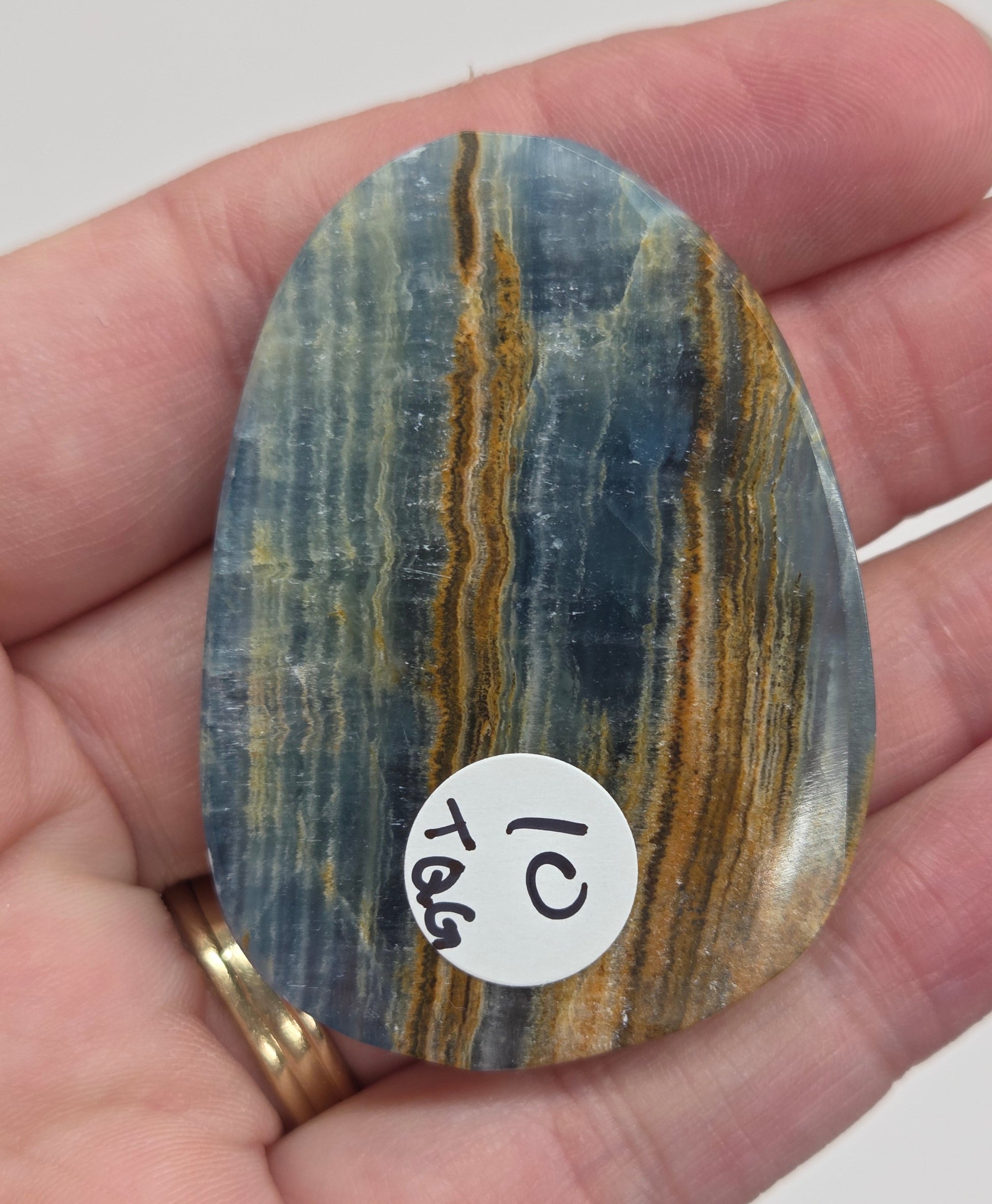 Blue Onyx cabochon with yellow veins held in a hand against a white background