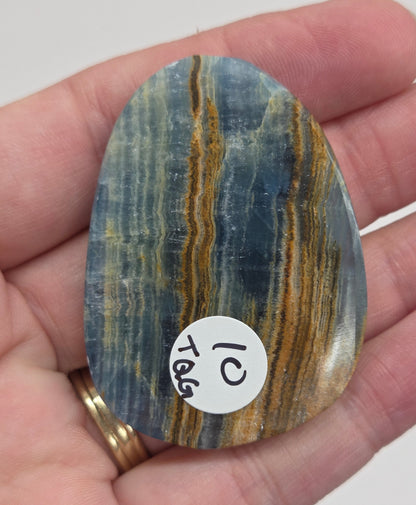 Blue Onyx cabochon with yellow veins held in a hand against a white background