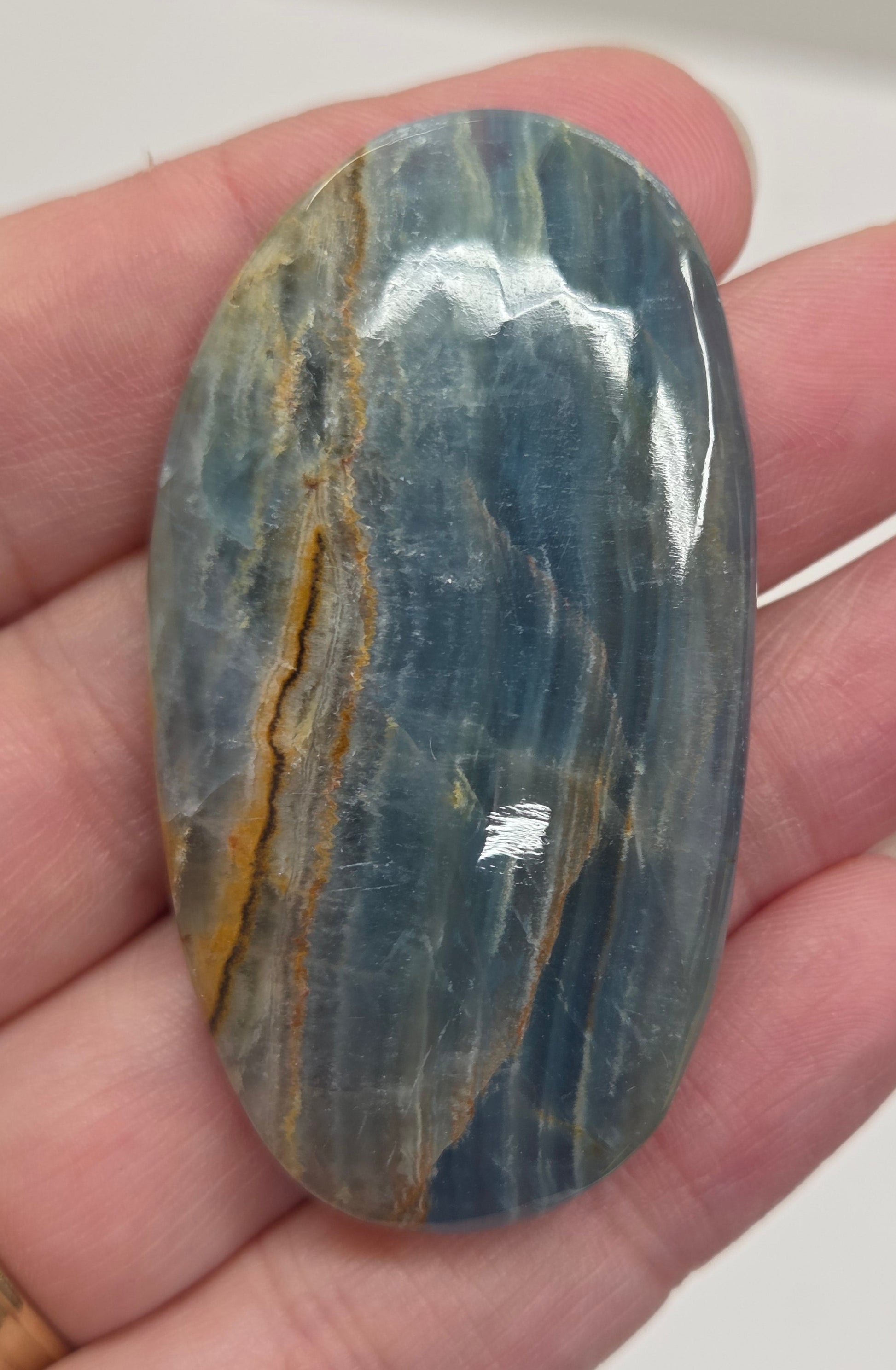Blue Onyx cabochon with yellow veins held in a hand against a white background