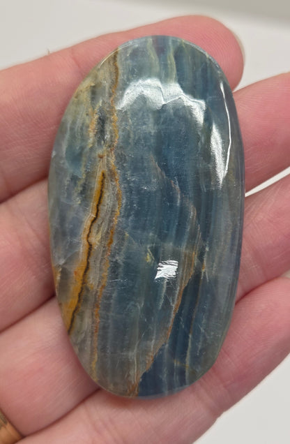 Blue Onyx cabochon with yellow veins held in a hand against a white background