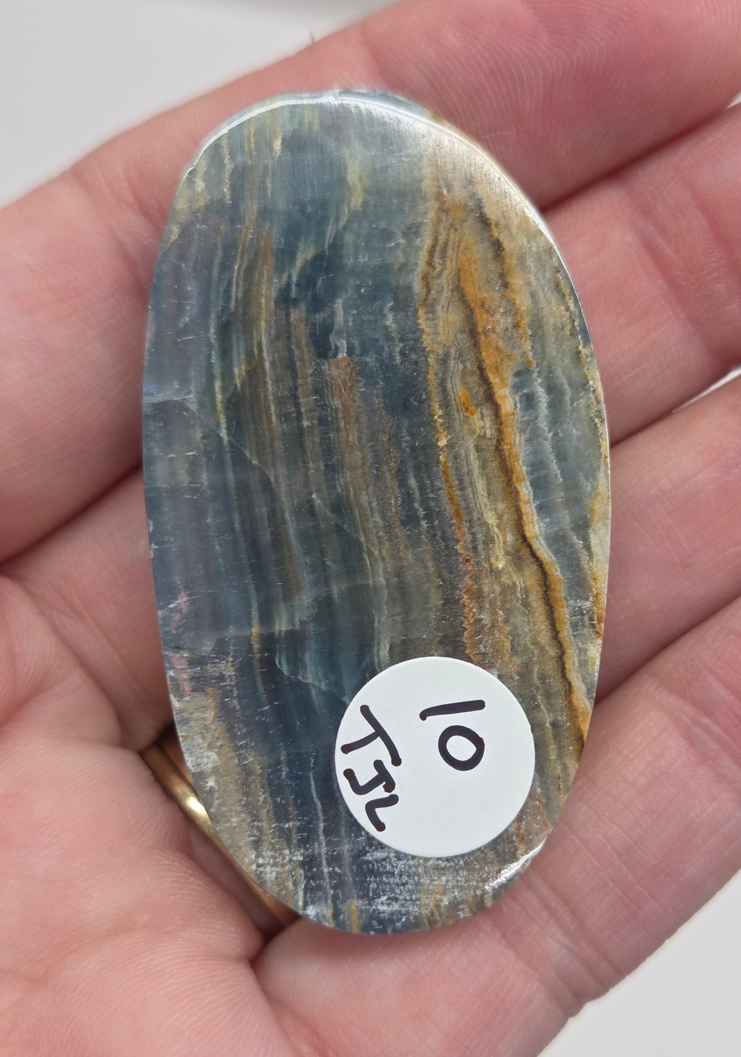 Blue Onyx cabochon with yellow veins held in a hand against a white background