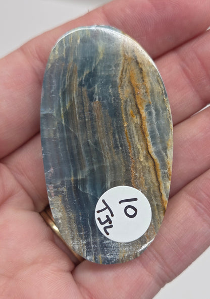 Blue Onyx cabochon with yellow veins held in a hand against a white background