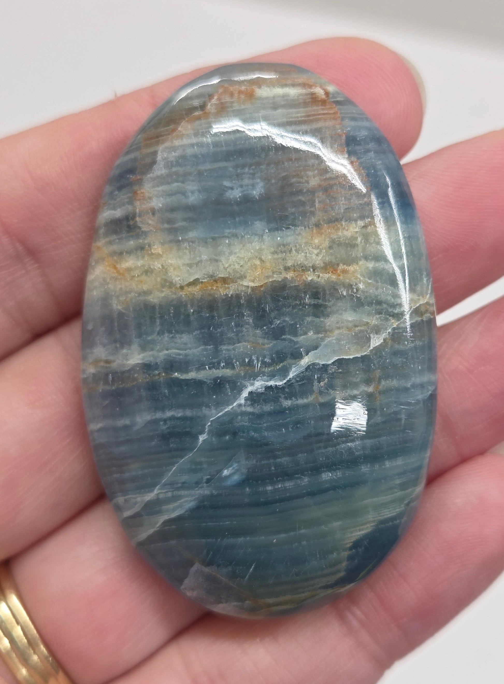 Blue Onyx cabochon with yellow veins held in a hand against a white background