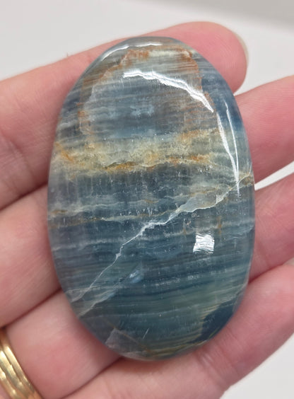 Blue Onyx cabochon with yellow veins held in a hand against a white background