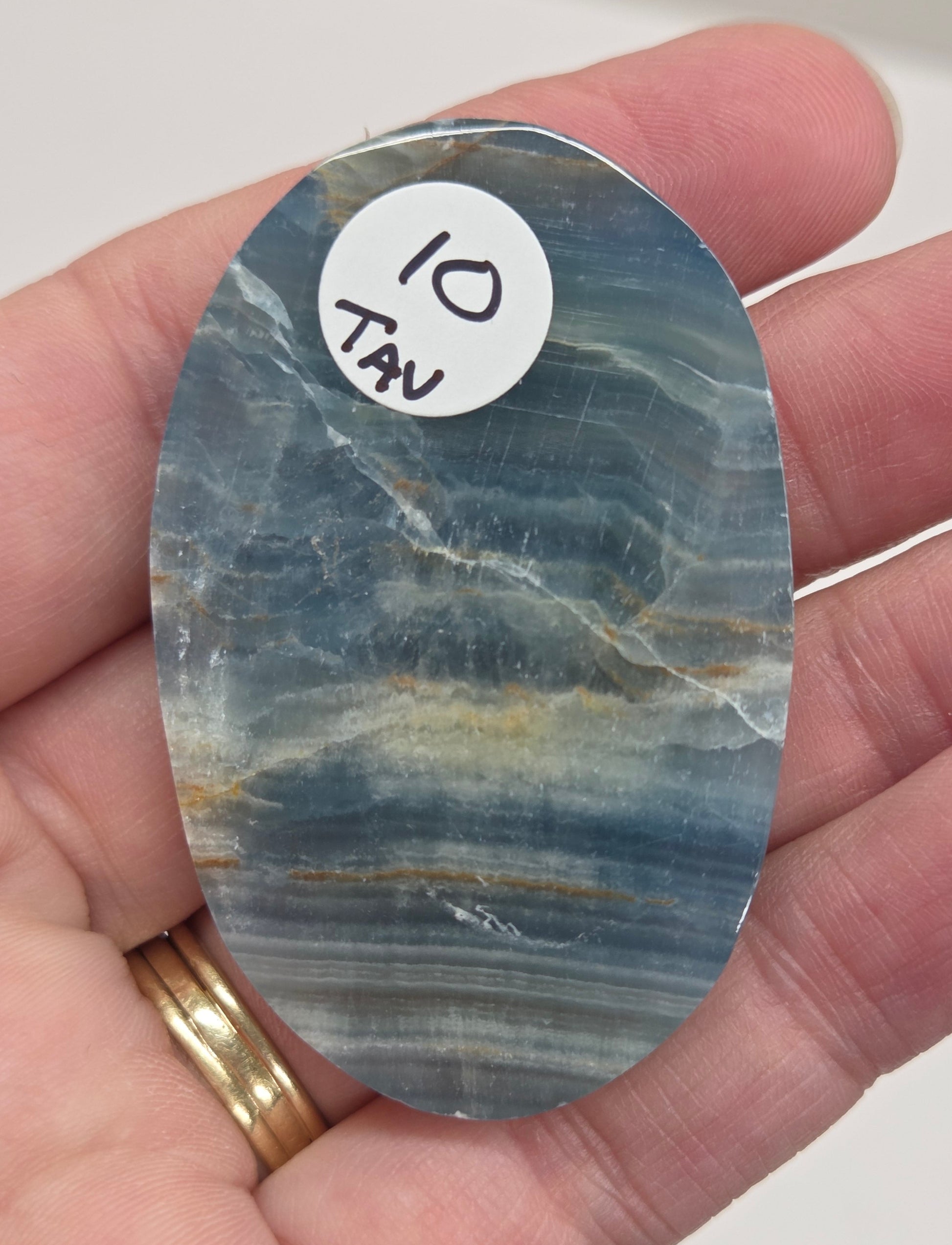 Blue Onyx cabochon with yellow veins held in a hand against a white background