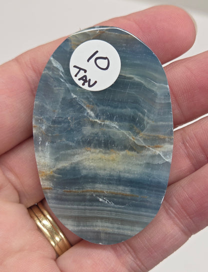 Blue Onyx cabochon with yellow veins held in a hand against a white background