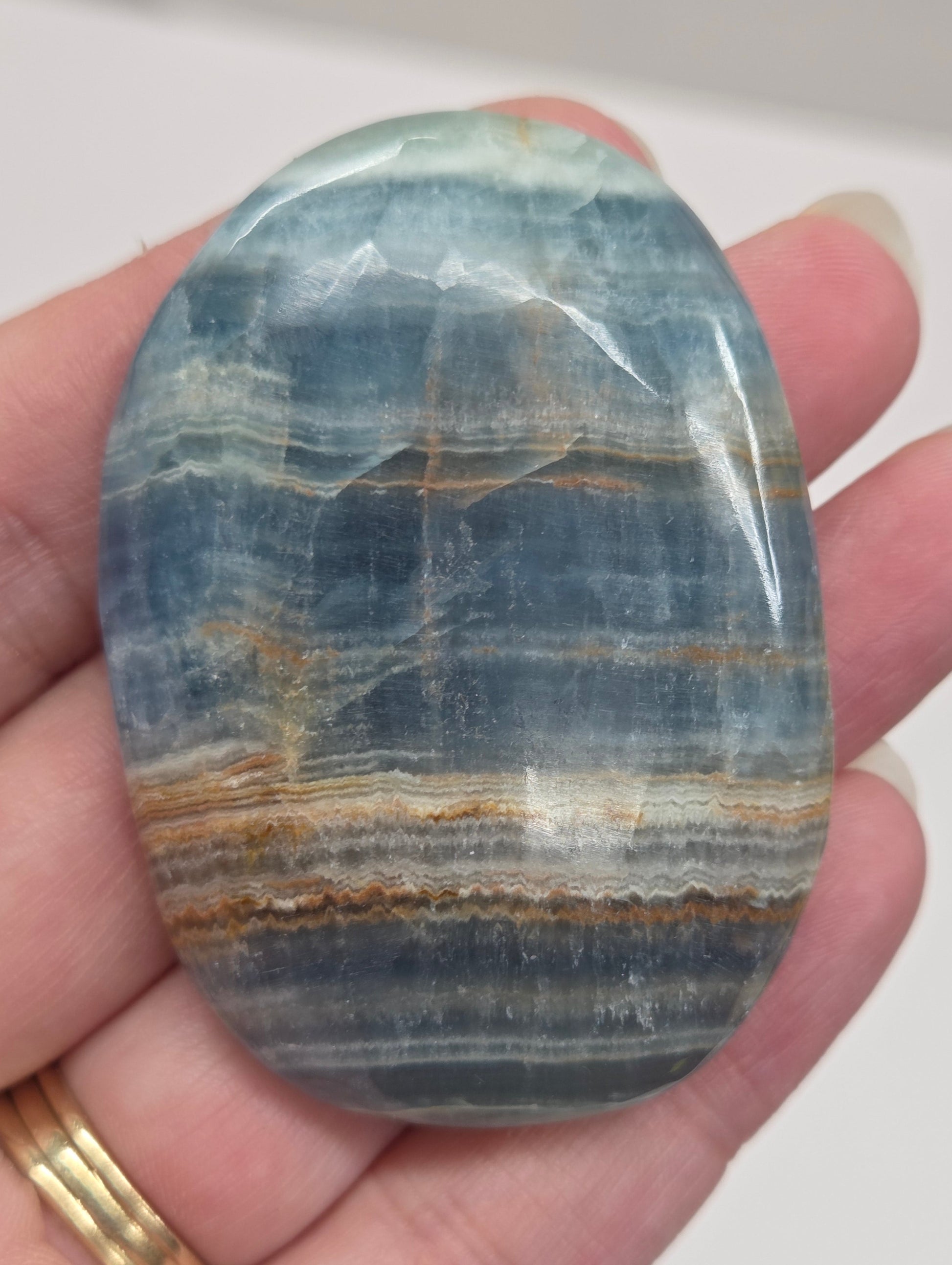 Blue Onyx cabochon with yellow veins held in a hand against a white background