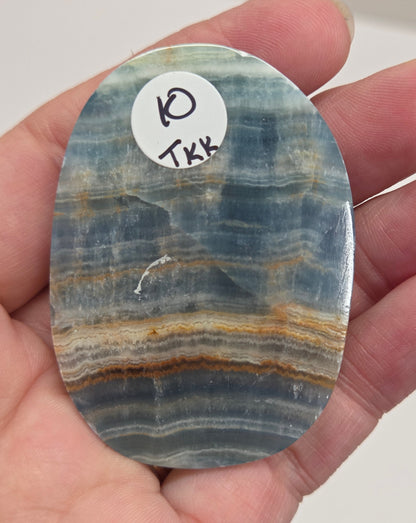 Blue Onyx cabochon with yellow veins held in a hand against a white background