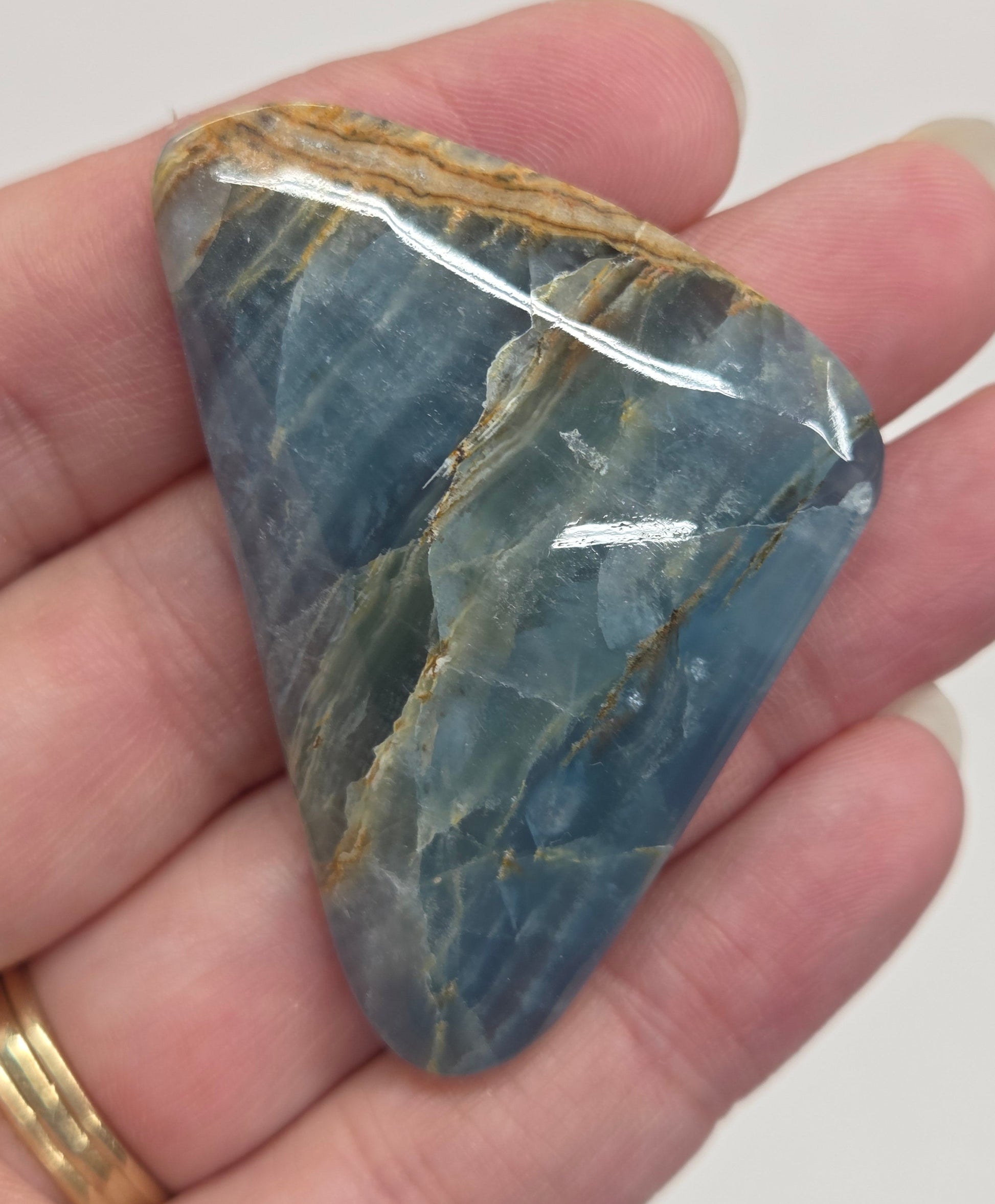 Blue Onyx cabochon with yellow veins held in a hand against a white background