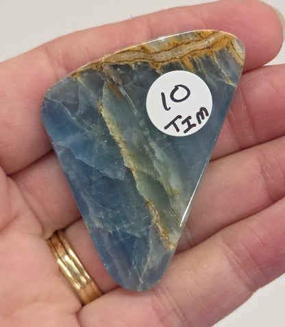 Blue Onyx cabochon with yellow veins held in a hand against a white background