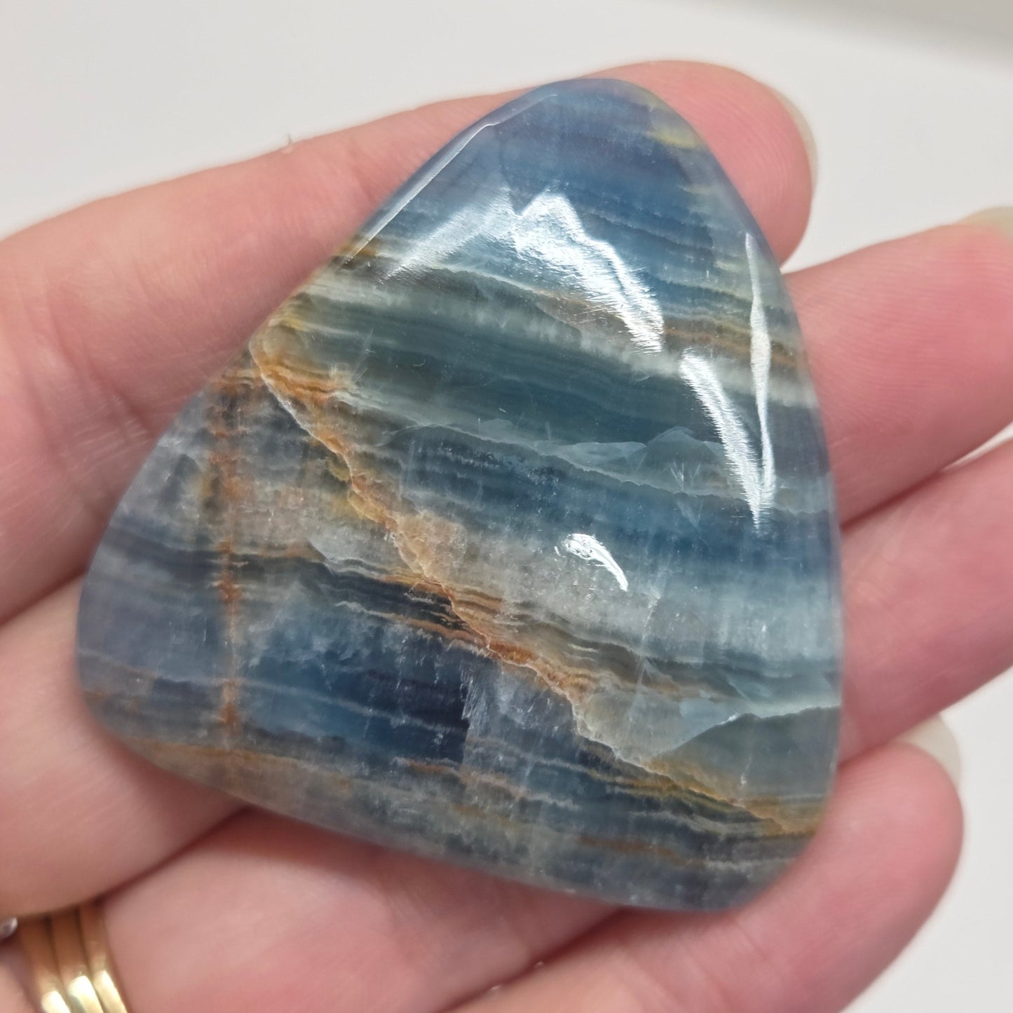 Blue Onyx cabochon with yellow veins held in a hand against a white background