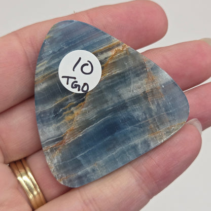 Blue Onyx cabochon with yellow veins held in a hand against a white background