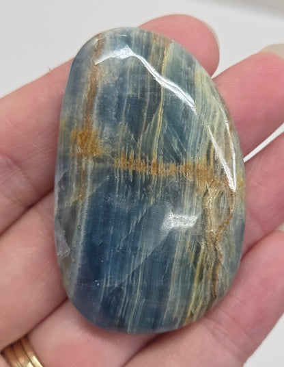 Blue Onyx cabochon with yellow veins held in a hand against a white background