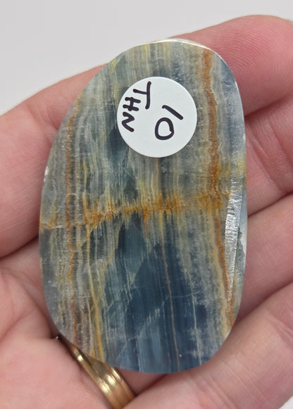 Blue Onyx cabochon with yellow veins held in a hand against a white background