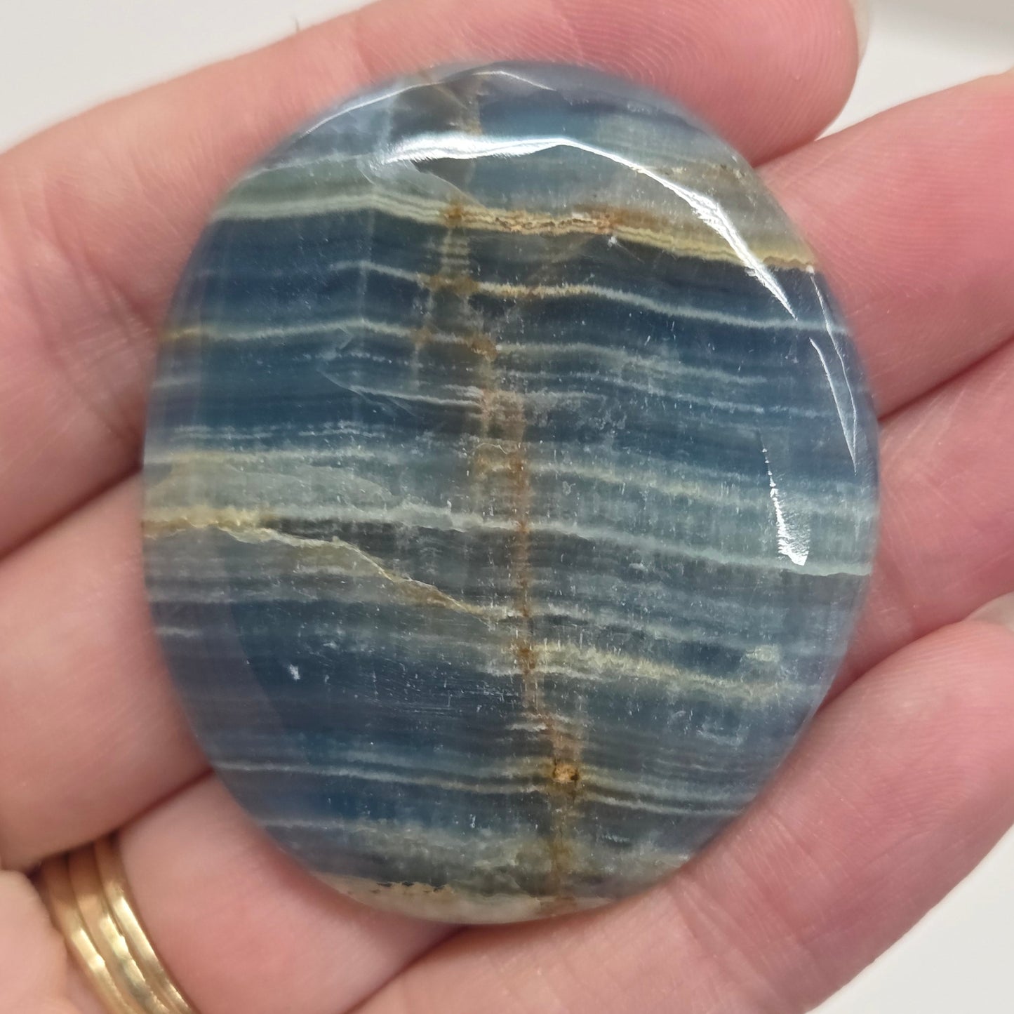 Blue Onyx cabochon with yellow veins held in a hand against a white background