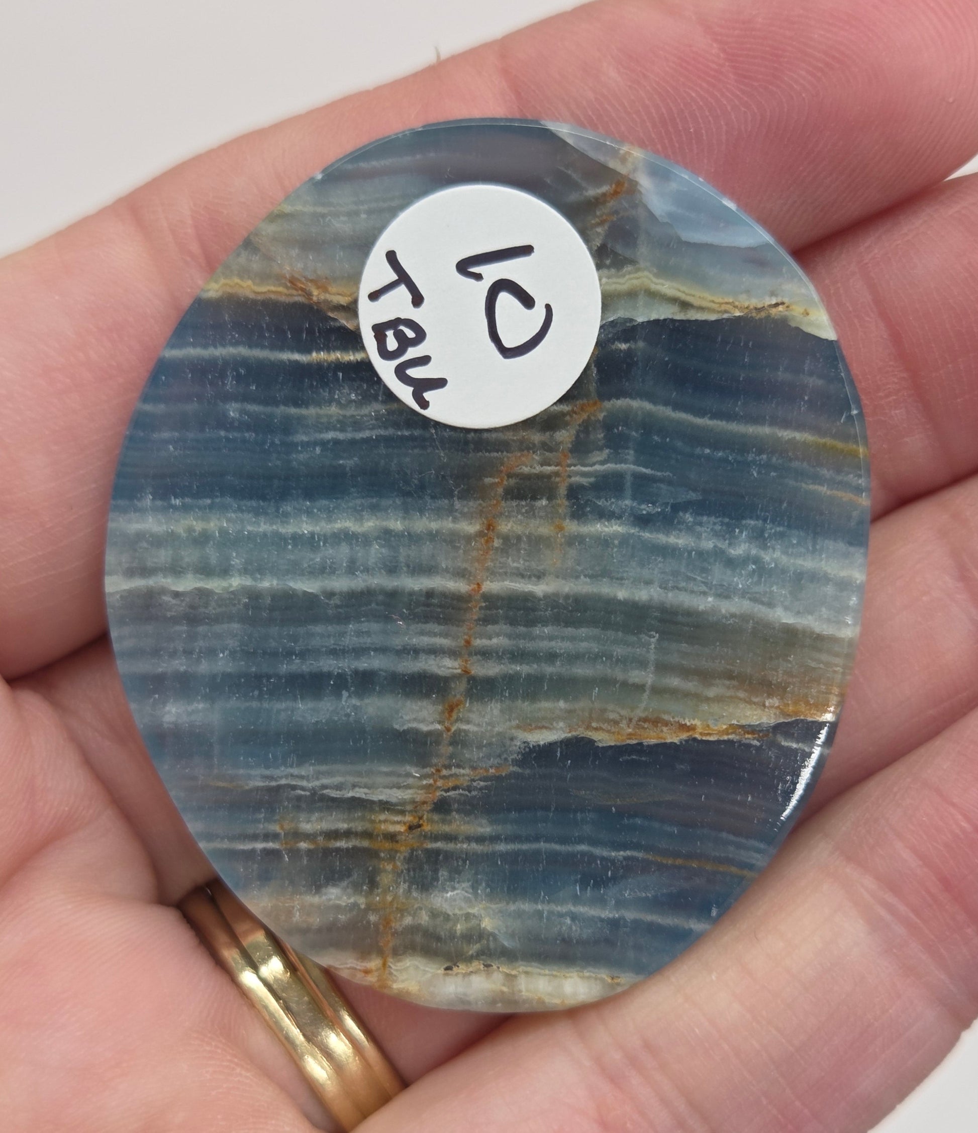 Blue Onyx cabochon with yellow veins held in a hand against a white background